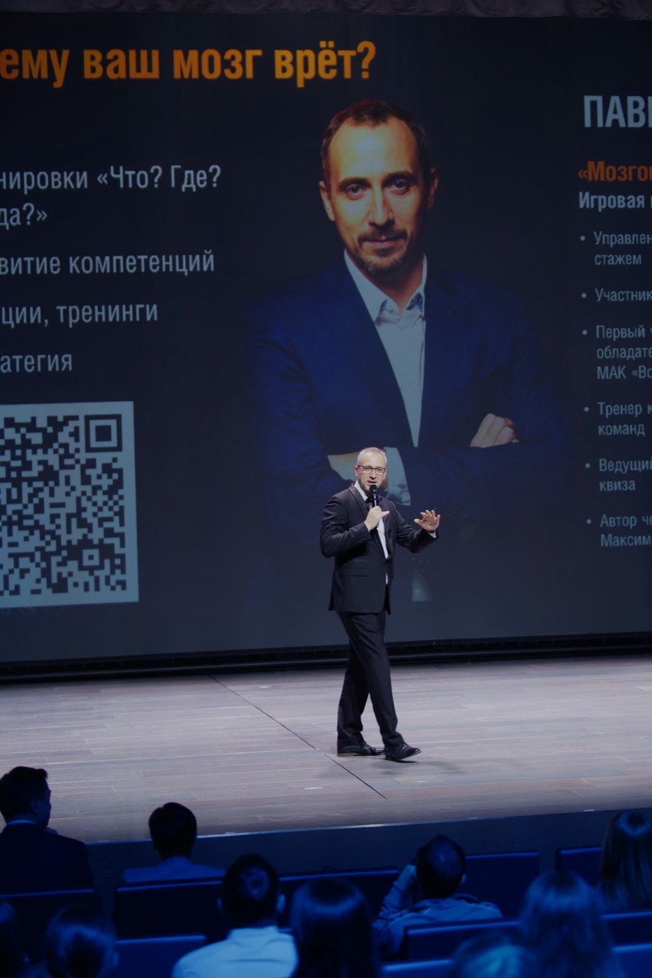 Павел Ершов с микрофоном на сцене театра, на экране позади — заставка выступления «Почему ваш мозг врёт?» с его портретом и именем