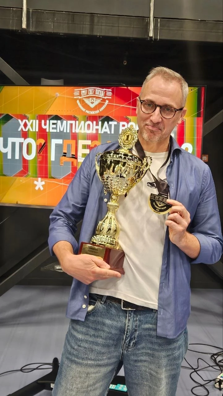 Павел Ершов держит кубок и золотую медаль на фоне баннера XXII чемпионата России по «Что? Где? Когда?»